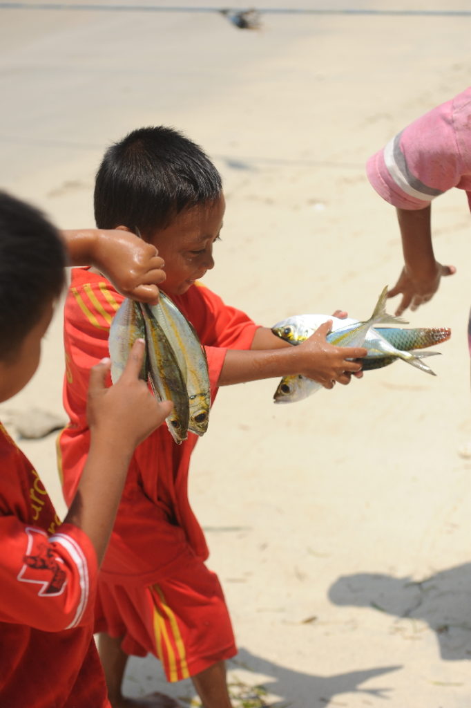 enfants avec des liasses de poissons dans les mains sur la plage de gili air