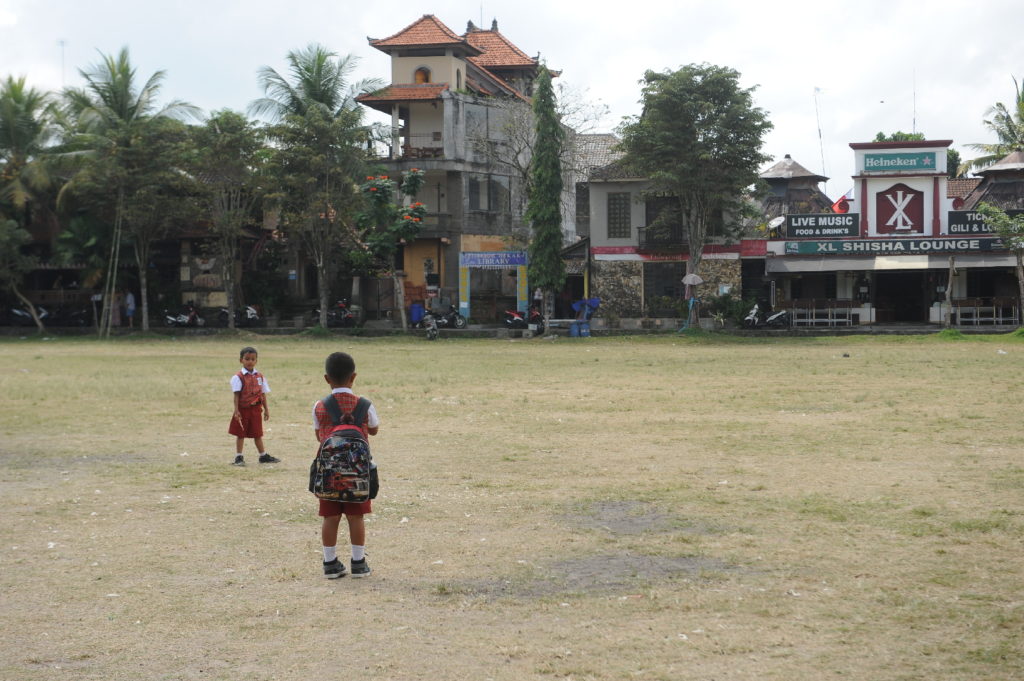 scène de vie dans les rues d'Ubud, enfants sur une place d'herbe