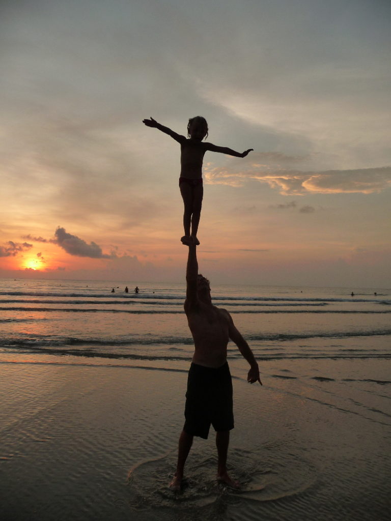 chatounette tient en équilibre sur les bras de Chaton au moment du coucher de soleil sur la plage de Kuta Bali