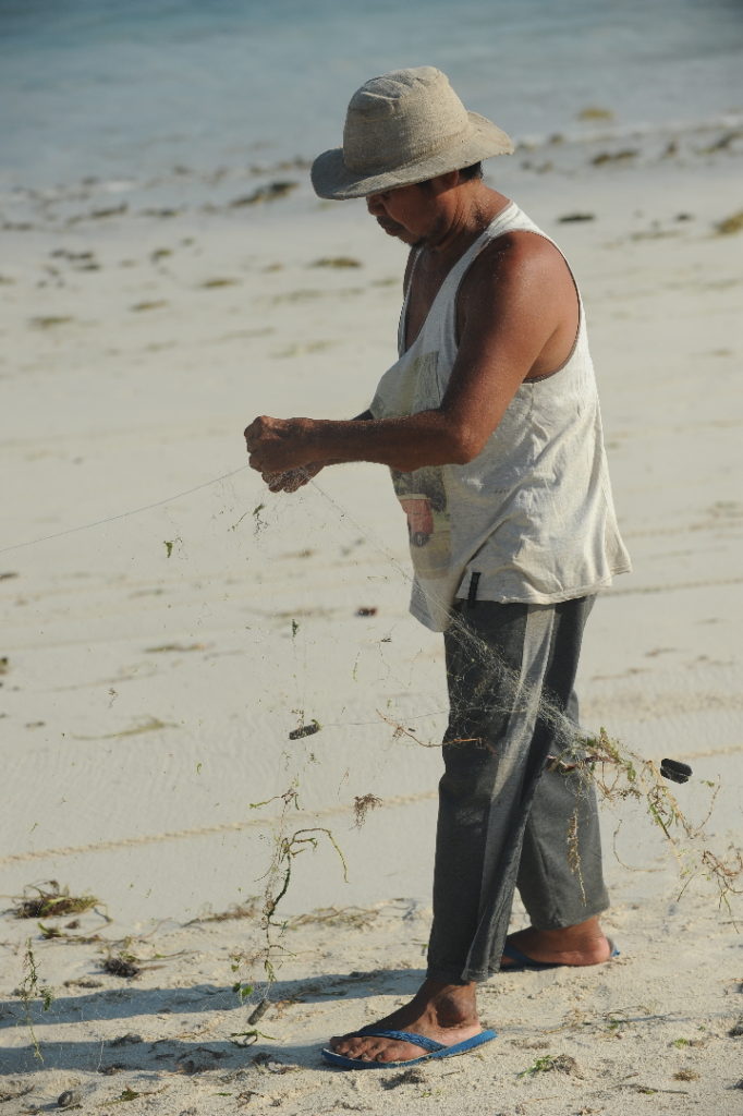 homme préparant son filet de pêche sur la plage de Tanjung Aan Beach