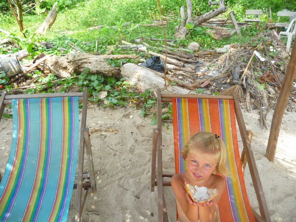 chatounette mange une noix de coco dans un transat sur "the best beach", la meilleure plage de koh lanta, derrière les détritus