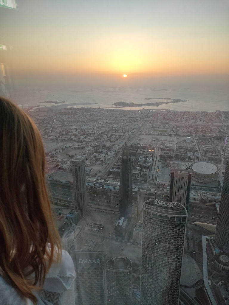 chatounette admire la vue depuis le 125 ème étage du burj khalifa, vers la mer au coucher du soleil, dubai